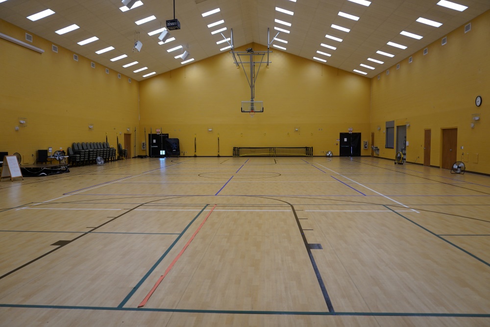 Full view of an empty indoor gymnasium with wood flooring and multiple court lines